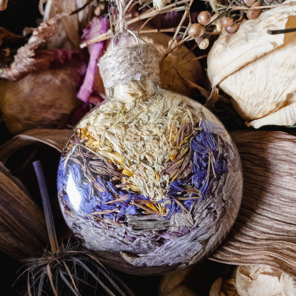 Flat, potion-bottle like glass sphere ornaments handmade and filled with dried flowers and grasses.